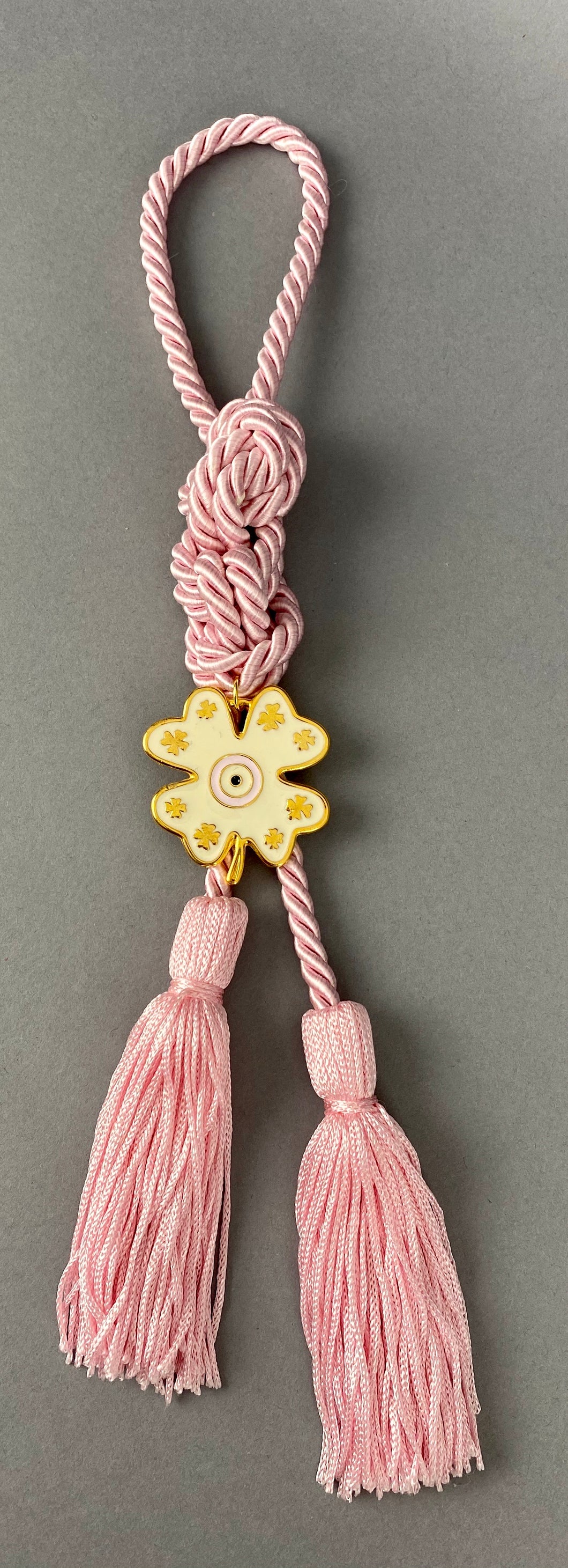Gouri 1023 Pearl Pink  Cord Gouri, metal 4 leaf clover with Mati and double tassel.   Measures 13” in length.